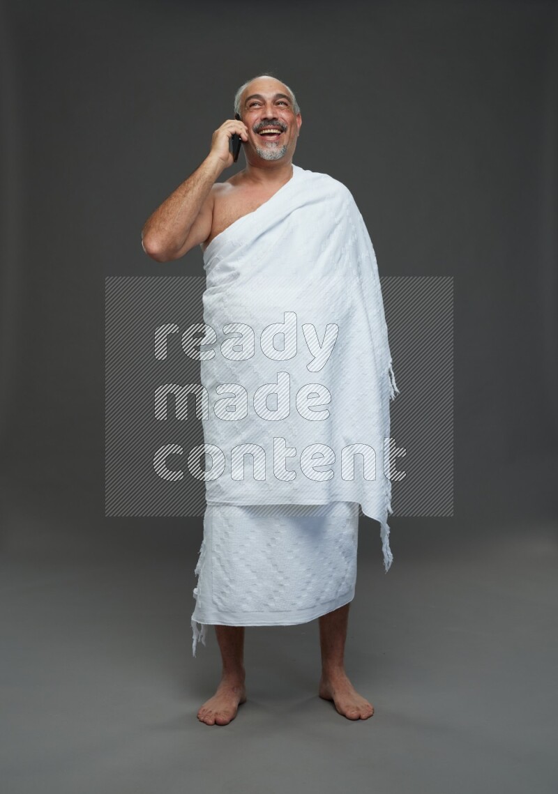 A man wearing Ehram Standing talking on phone on gray background