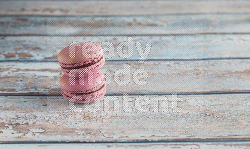 45º Shot of two Purple Strawberry macarons on light blue wooden background