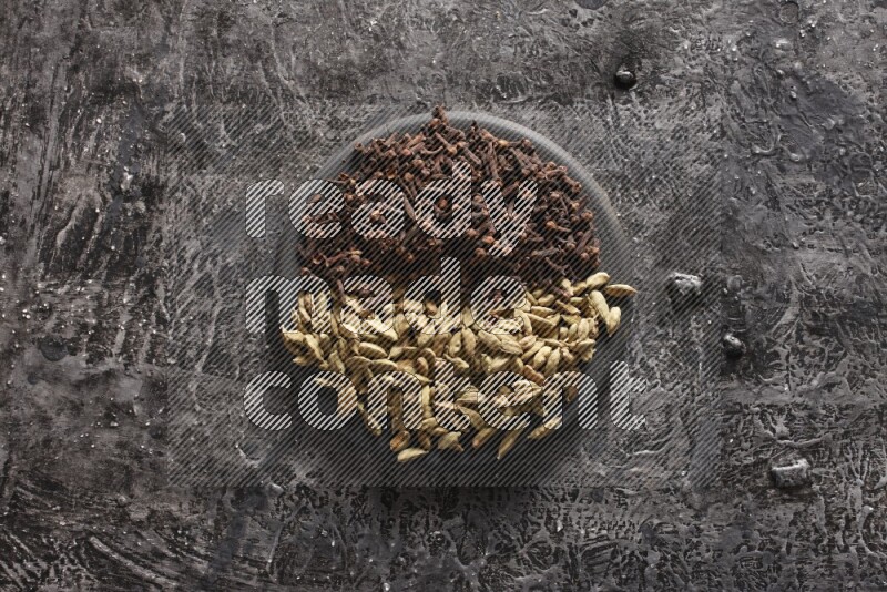Cardamom and cloves on a black plate on textured black background
