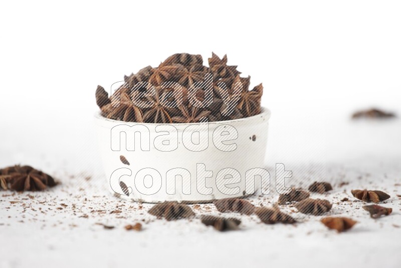 Star Anise in a white bowl and more of it sprinkled on white background