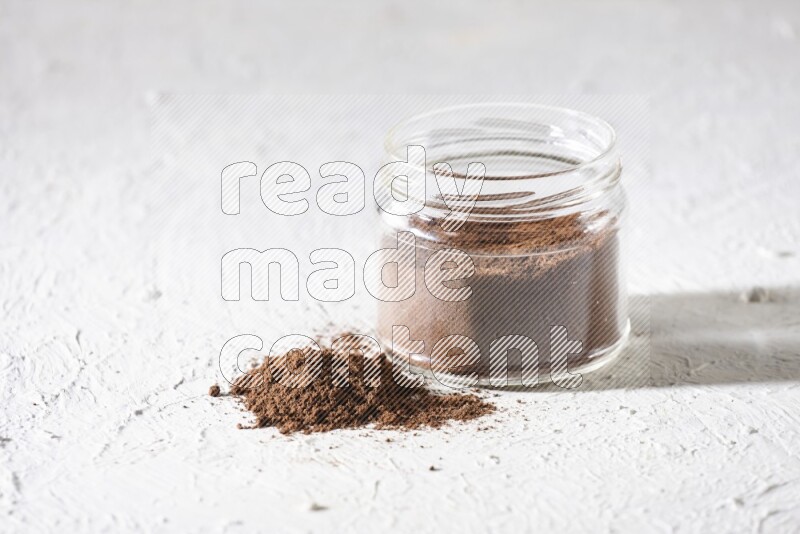 A glass jar full of cloves powder on a textured white flooring