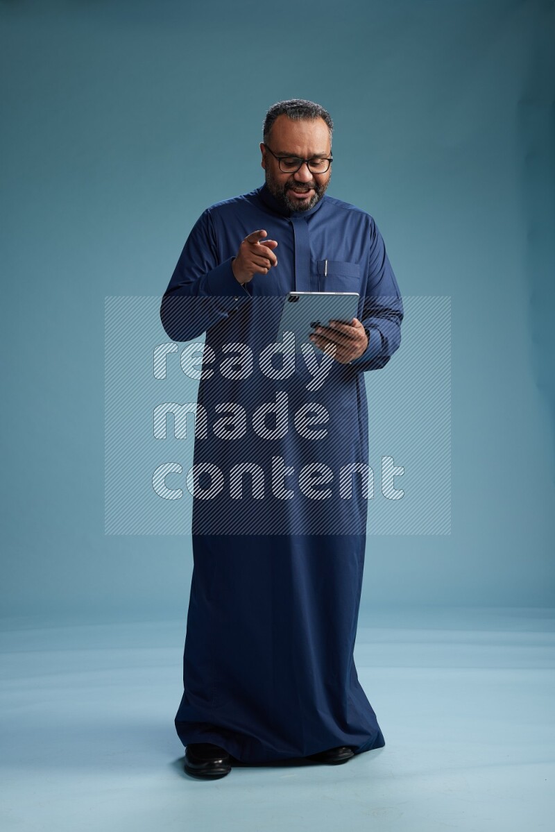 Saudi Man without shimag Standing working on tablet on blue background