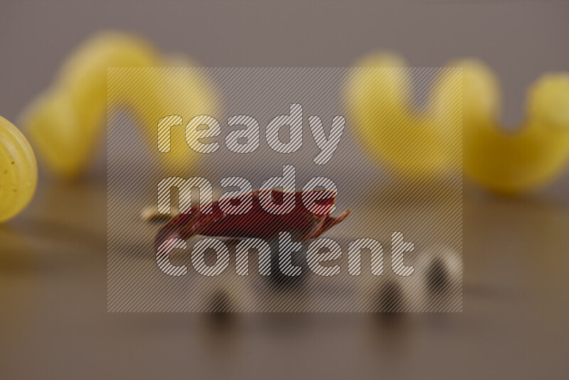 Raw pasta with different ingredients such as cherry tomatoes, garlic, onions, red chilis, black pepper, white pepper, bay laurel leaves, rosemary and cardamom on beige background