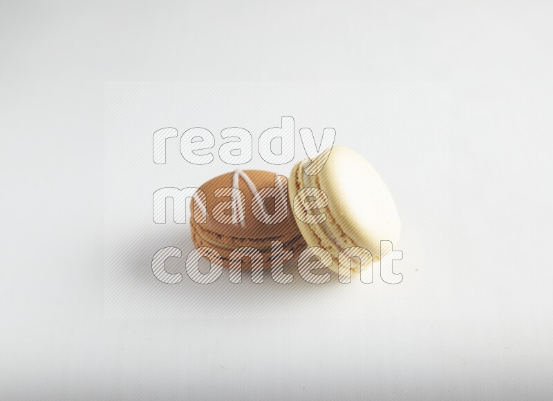 45º Shot of of two assorted Brown Irish Cream, and Yellow Vanilla macarons on white background