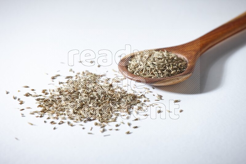 A wooden ladle full of cumin seeds on a white flooring