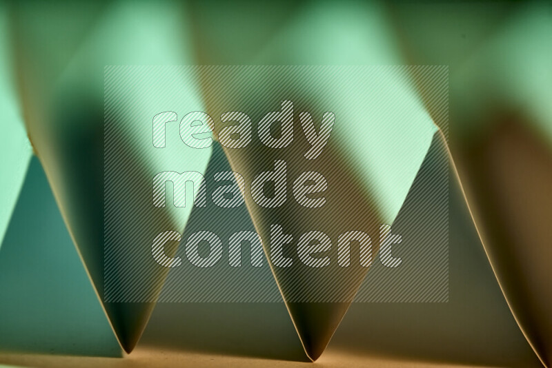 A close-up abstract image showing sharp geometric paper folds in green gradients and warm tones