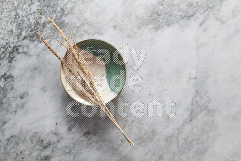 Wheat stalks on multicolored pottery plate on grey marble background