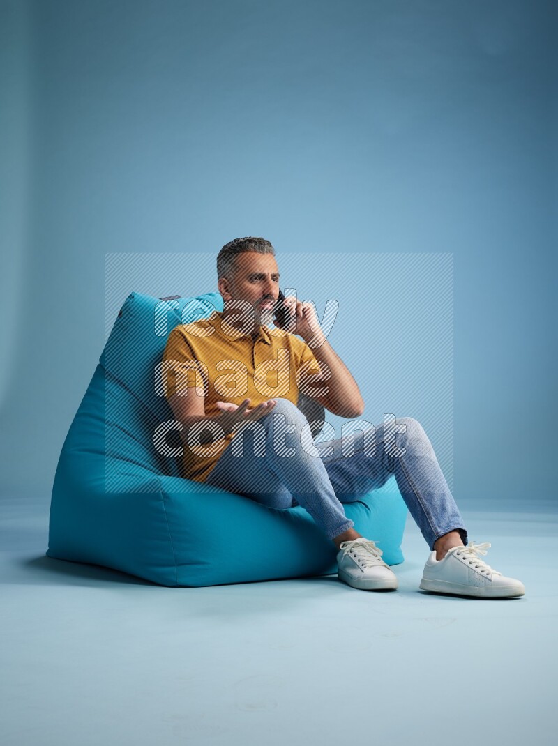 A man sitting on a blue beanbag and talking on the phone
