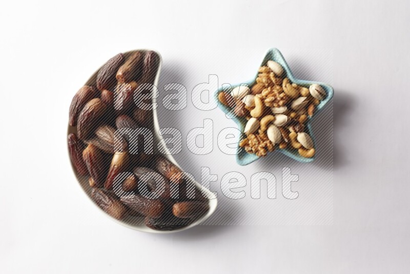 Dates in a crescent pottery plate and a star shaped plate with mixed nuts on white background