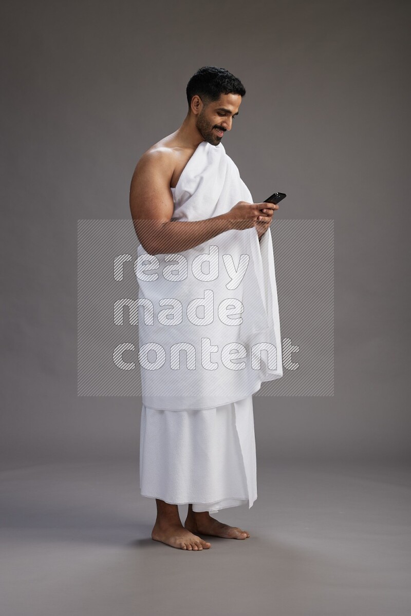 A man wearing Ehram Standing texting on phone on gray background