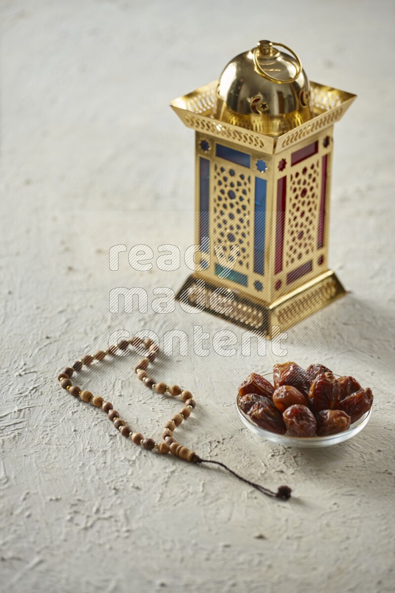 A golden lantern with different drinks, dates, nuts, prayer beads and quran on textured white background