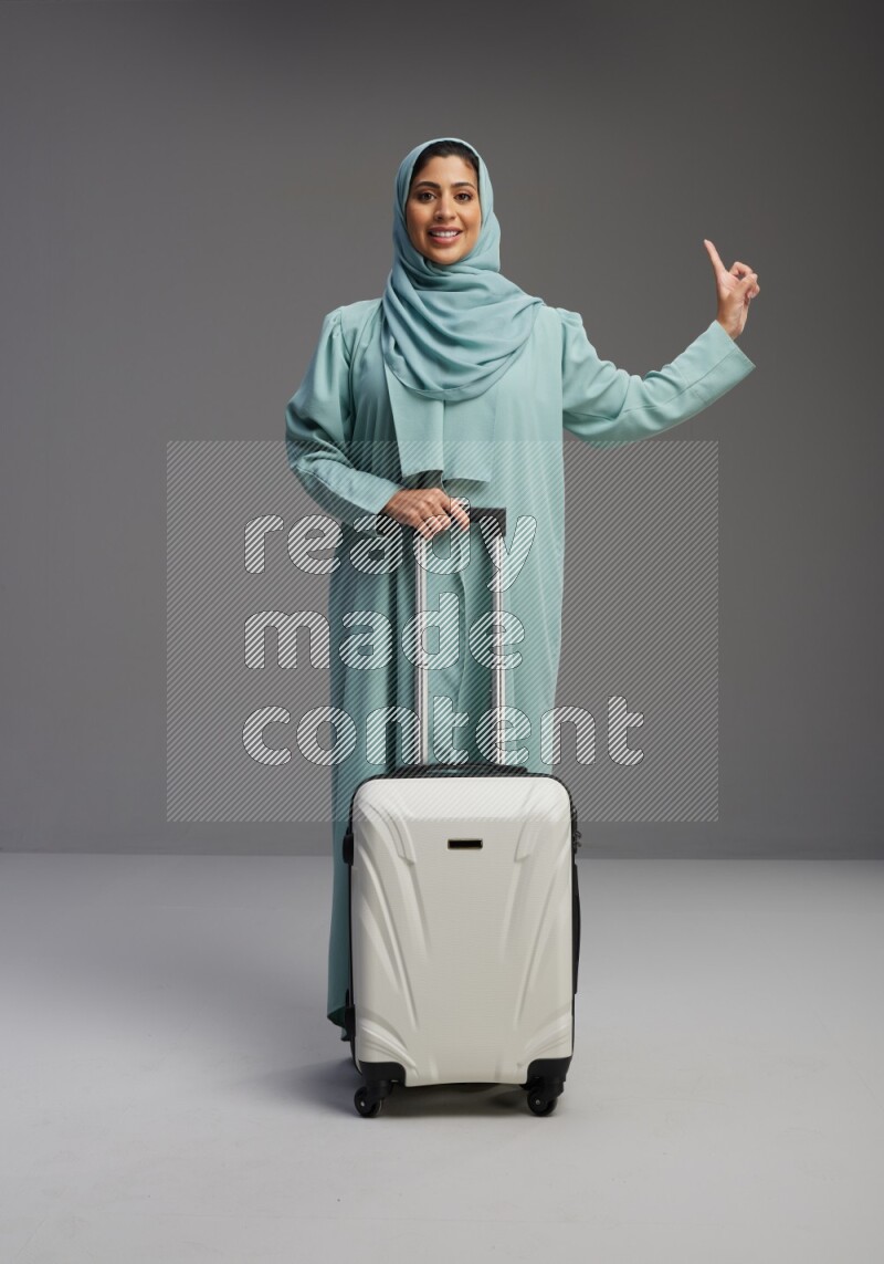 Saudi Woman wearing Abaya standing holding Travel bag on Gray background