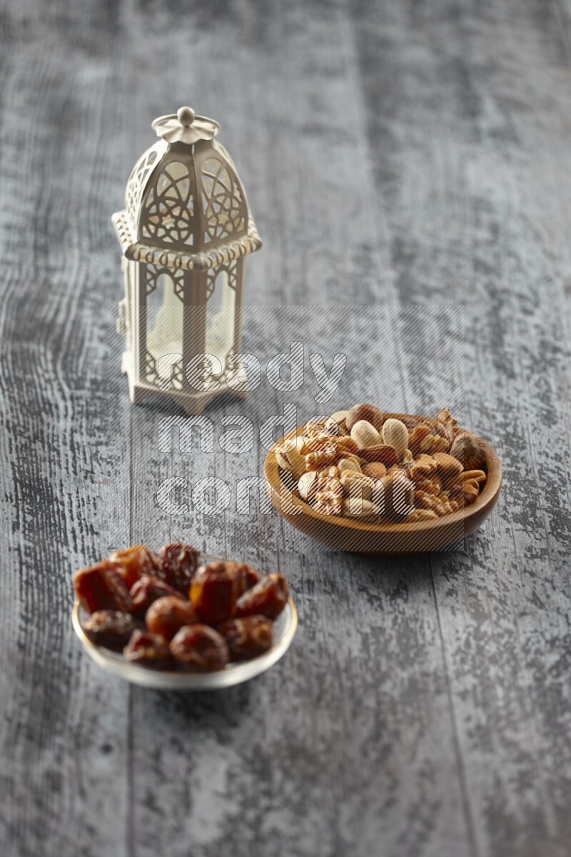 A white lantern with different drinks, dates, nuts, prayer beads and quran on grey wooden background