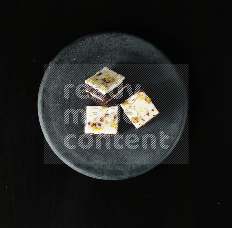 Assorted desserts in a black pottery plate on black background