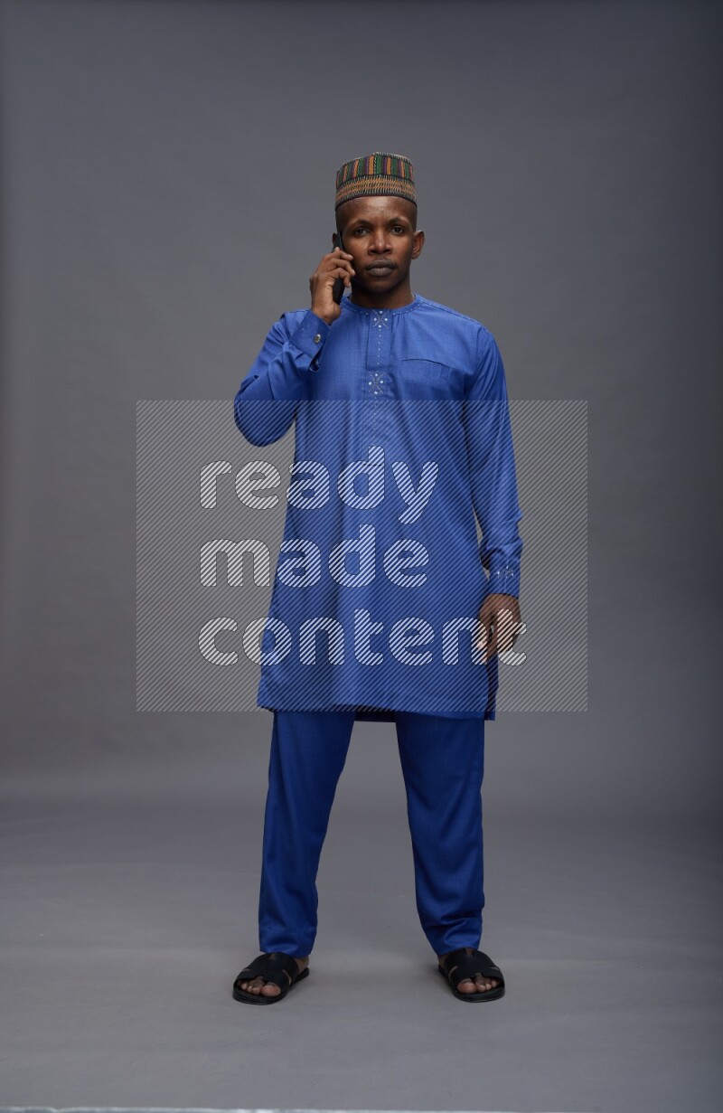 Man wearing Nigerian outfit standing talking on phone on gray background