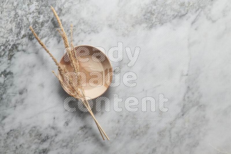 Wheat stalks on multicolored pottery plate on grey marble background