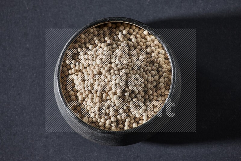 Black pottery bowl full of white pepper on black flooring