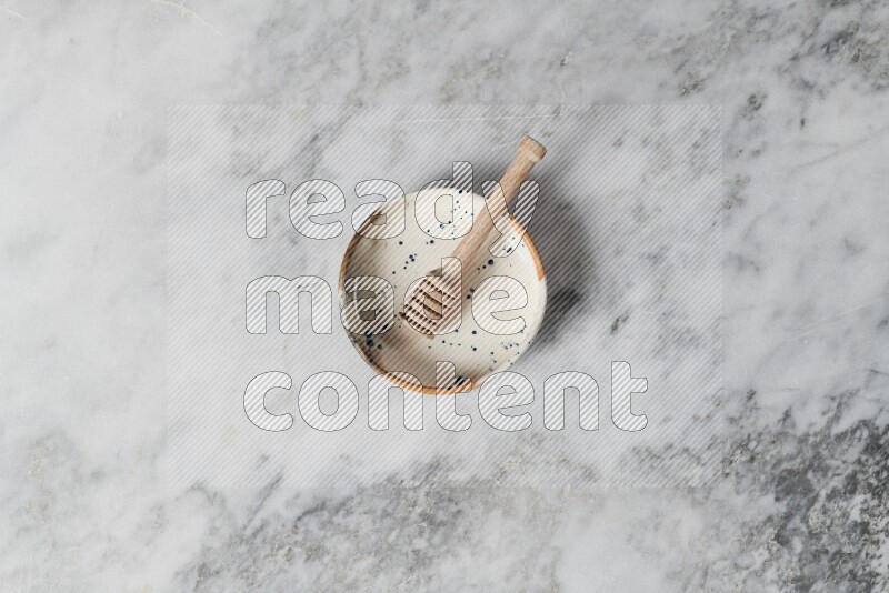 Multicolored pottery bowl with wooden honey dipper in it on grey marble background