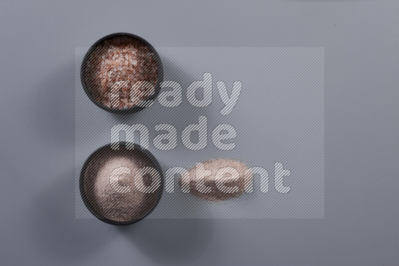 2 وعاء فخاري احدهمها ممتلئ بملح الهيمالايا الناعم والأخر بملح الهيمالايا الخشن على خلفية رمادية