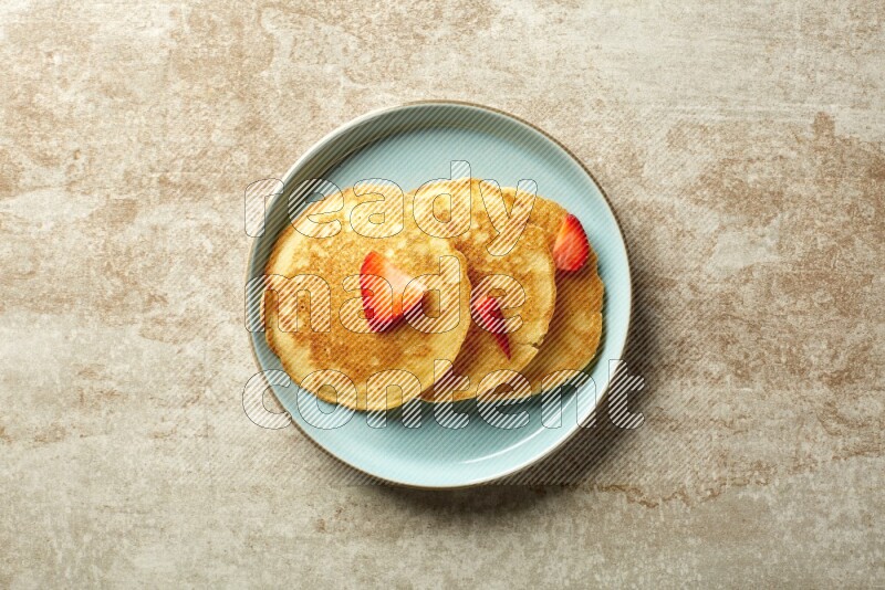 Three stacked strawberry pancakes in a blue plate on beige background