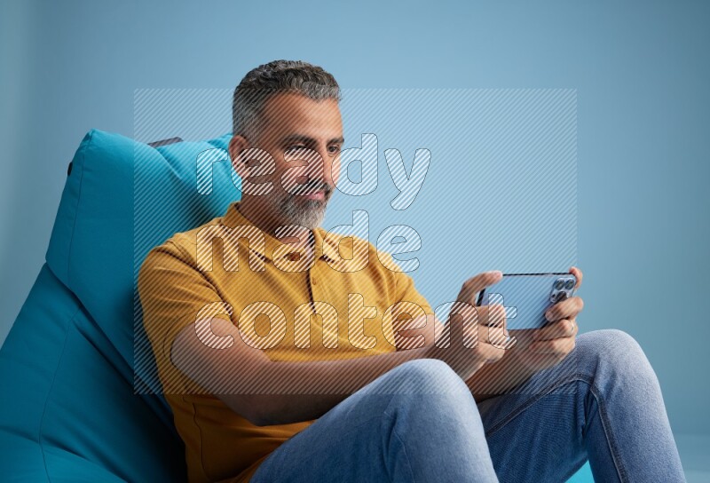A man sitting on a blue beanbag and playing on phone