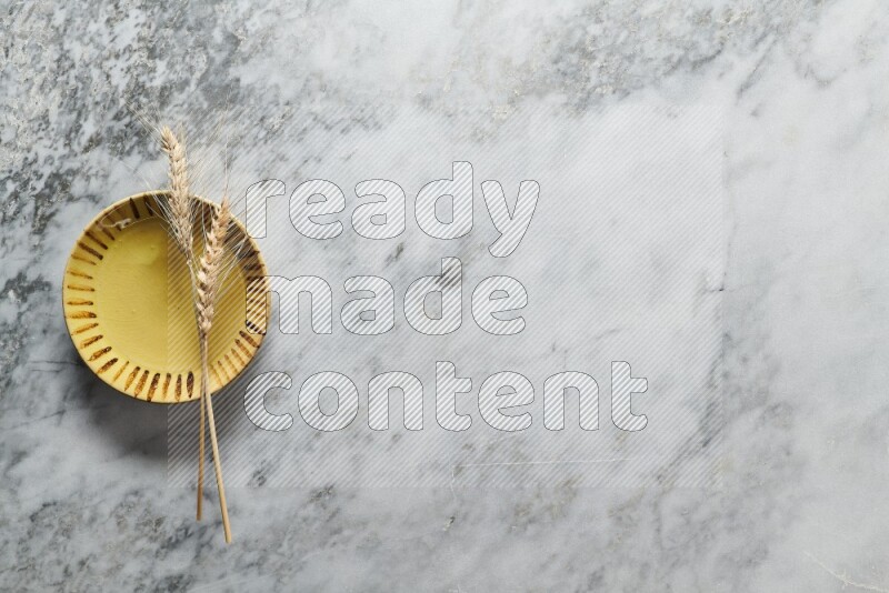 Wheat stalks on multicolored pottery plate on grey marble background