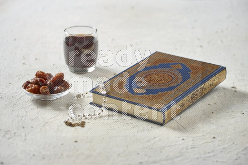 Quran with dates, prayer beads and different drinks all placed on textured white background