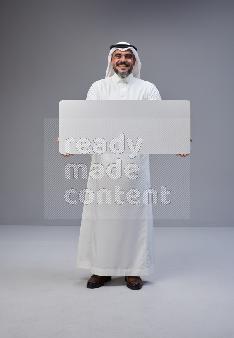 Saudi man Wearing Thob and white Shomag standing holding board on Gray background
