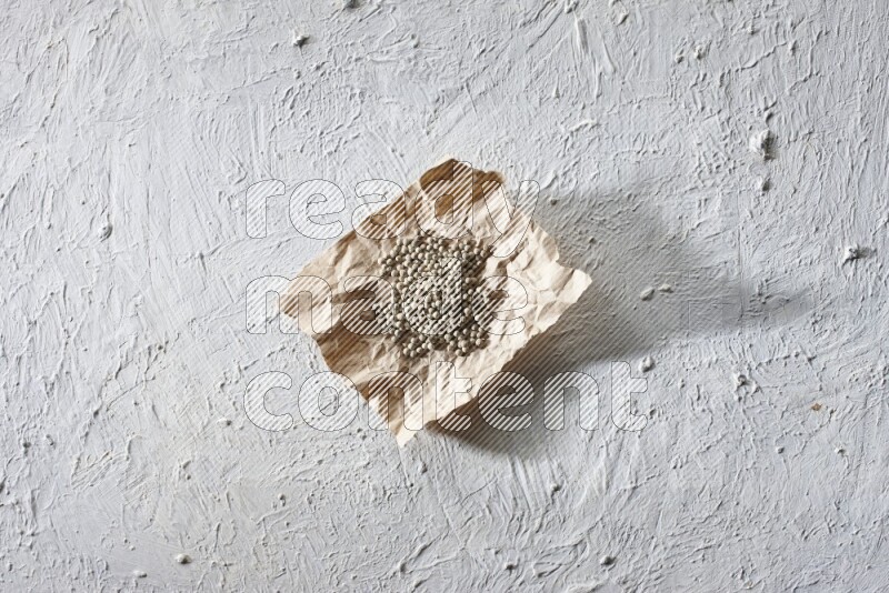 White pepper beads in a crumpled piece of paper on textured white flooring