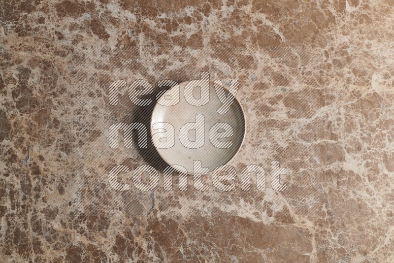 A beige pottery plate on beige marble background