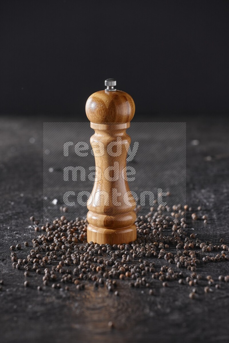 A wooden grinder with black pepper beads on a textured black flooring