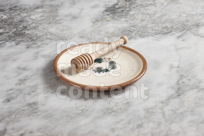 Decorative pottery plate with wooden honey dipper in it on grey marble background
