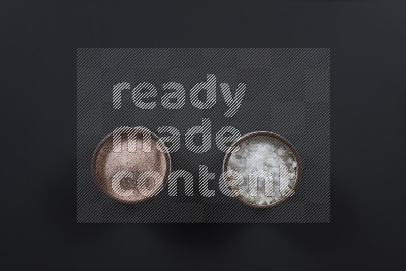 2 pottery bowls one is filled with himalayan salt and the other with white salt on black background