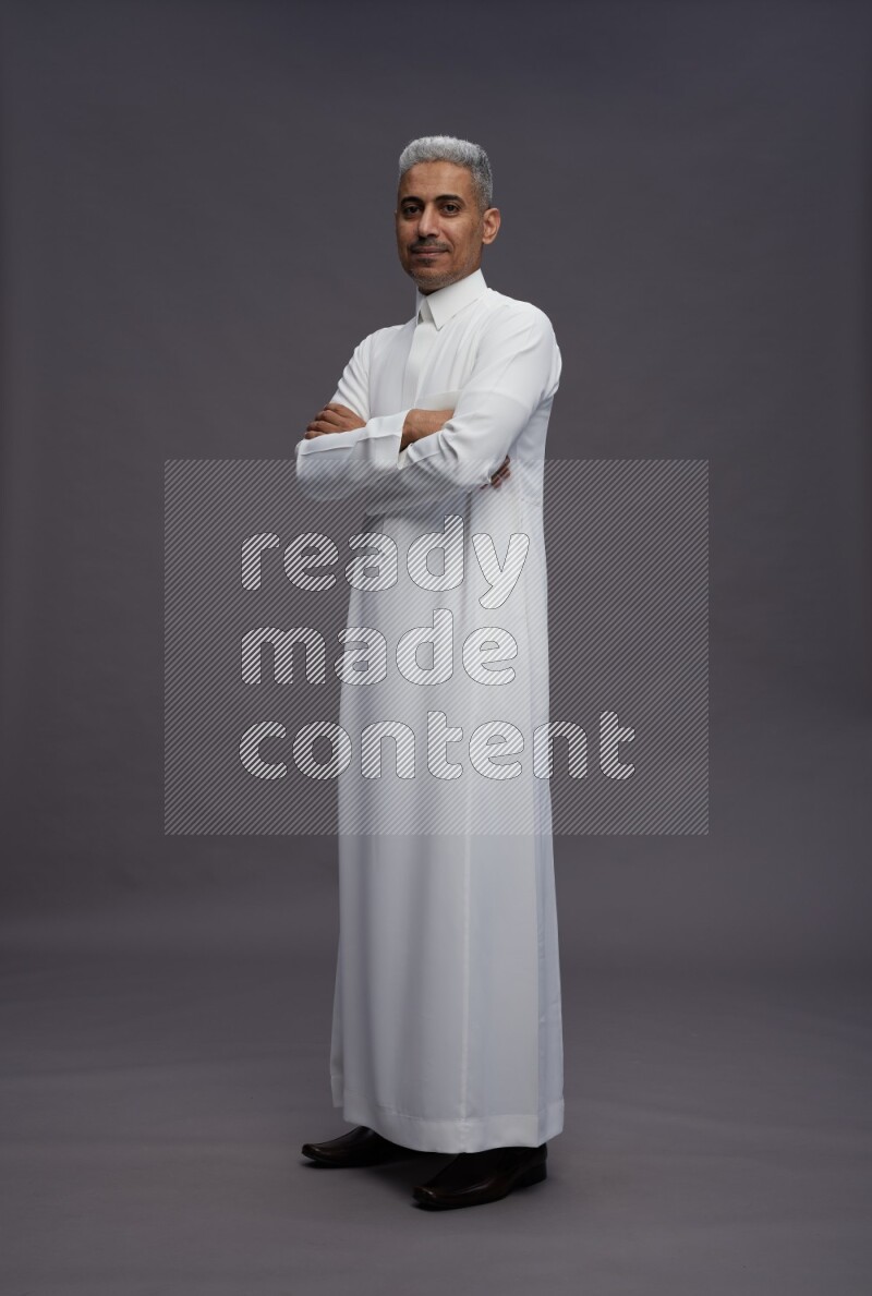 Saudi man wearing thob standing with crossed arms on gray background