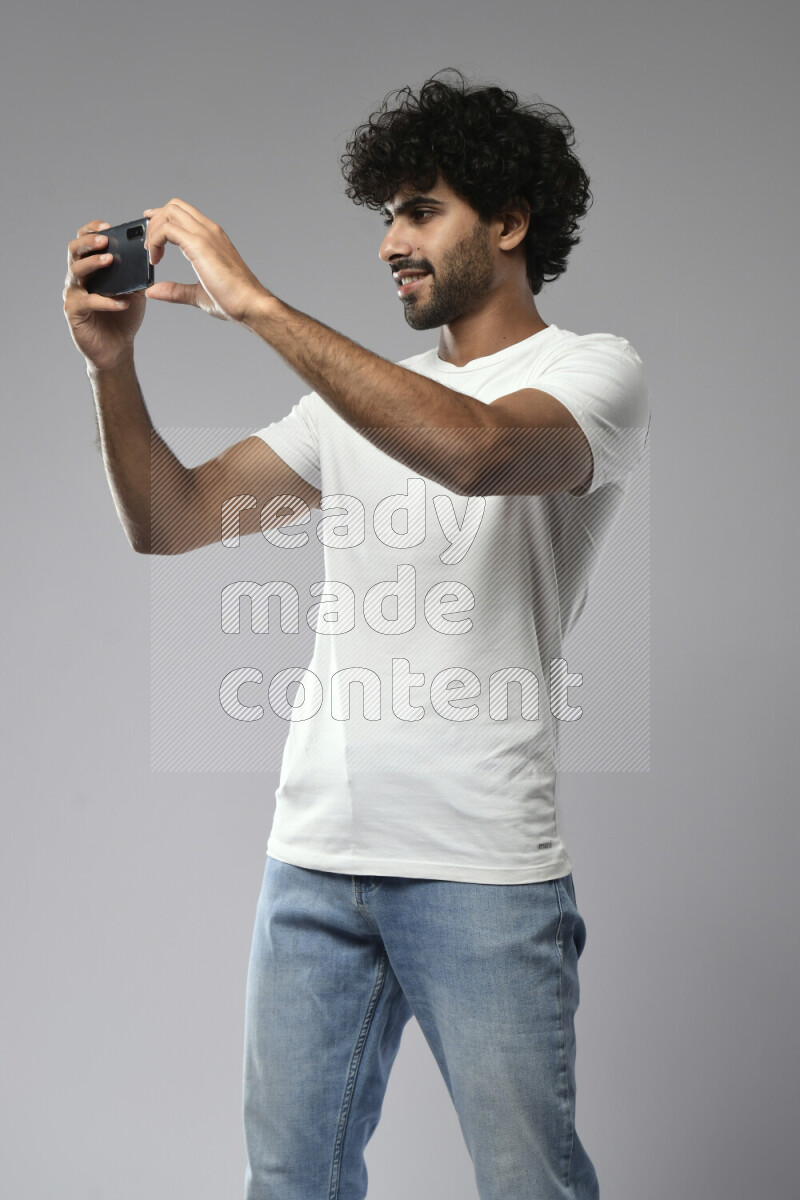 A man wearing casual standing and shooting with his phone on white background