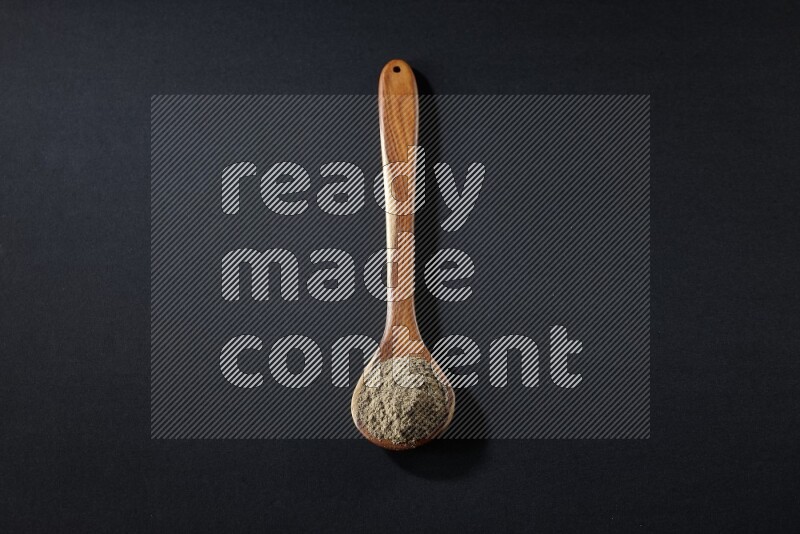 A wooden ladle full of cardamom powder on black flooring