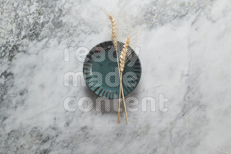 Wheat stalks on multicolored pottery plate on grey marble background