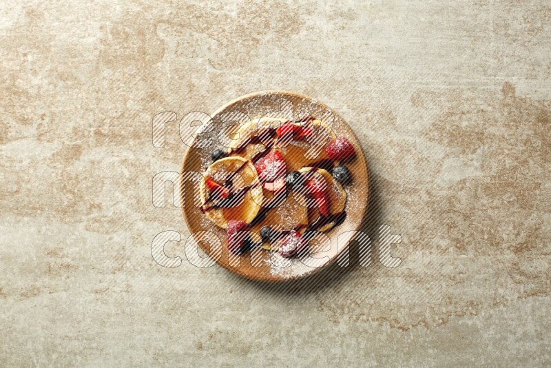 Five stacked mixed berries mini pancakes in a brown plate on beige background