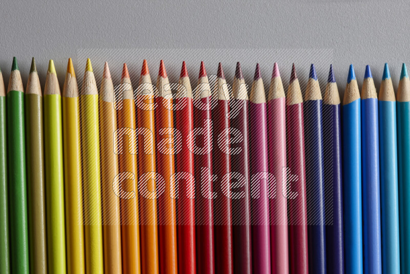 A collection of colored pencils arranged showcasing a gradient of different hues on grey background