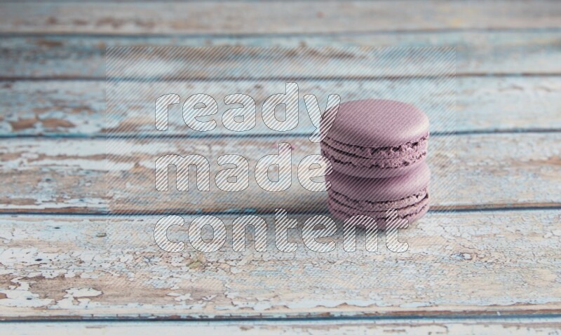 45º Shot of two Purple Blueberry macarons on light blue wooden background