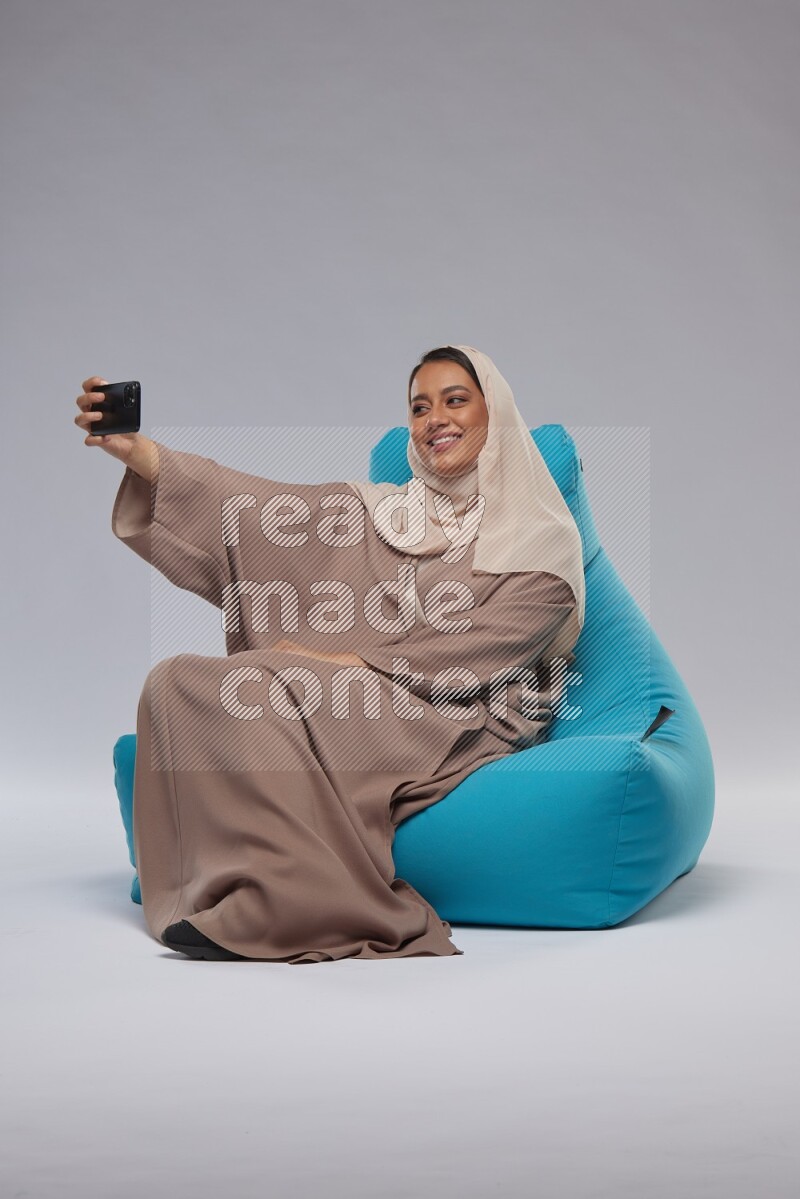 A Saudi woman sitting on a blue beanbag and taking selfie