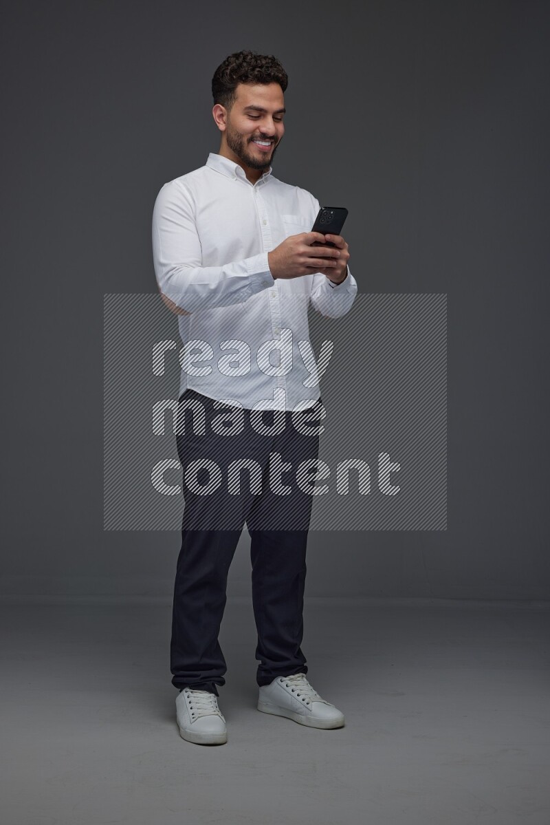 A man wearing smart casual standing and using his phone eye level on a gray background