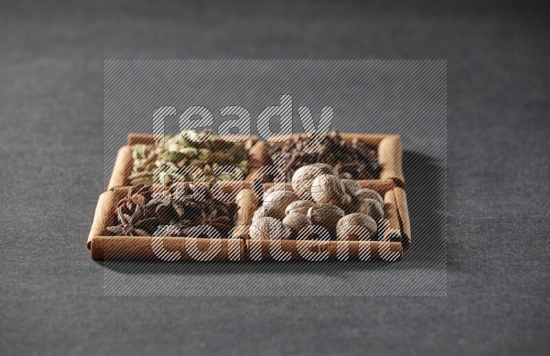 4 squares of cinnamon sticks full of cardamom, star anise, nutmegs and cloves on black flooring