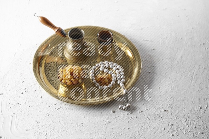 Raisins in a metal bowl with coffee and prayer beads on a tray in a light setup