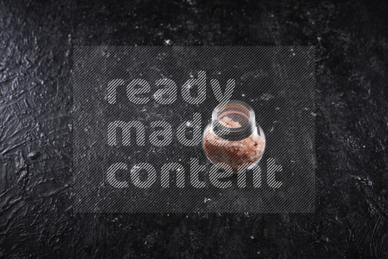 A glass jar full of coarse himalayan salt crystals on black background
