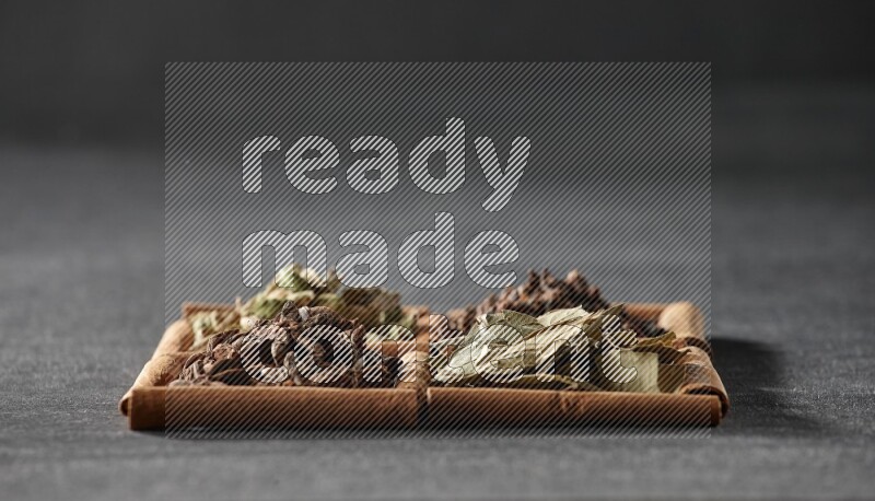 4 مربعات من عيدان القرفة ممتلئة باليانسون النجمي وحبوب الهيل والقرنفل وأوراق الغار على أرضية سوداء