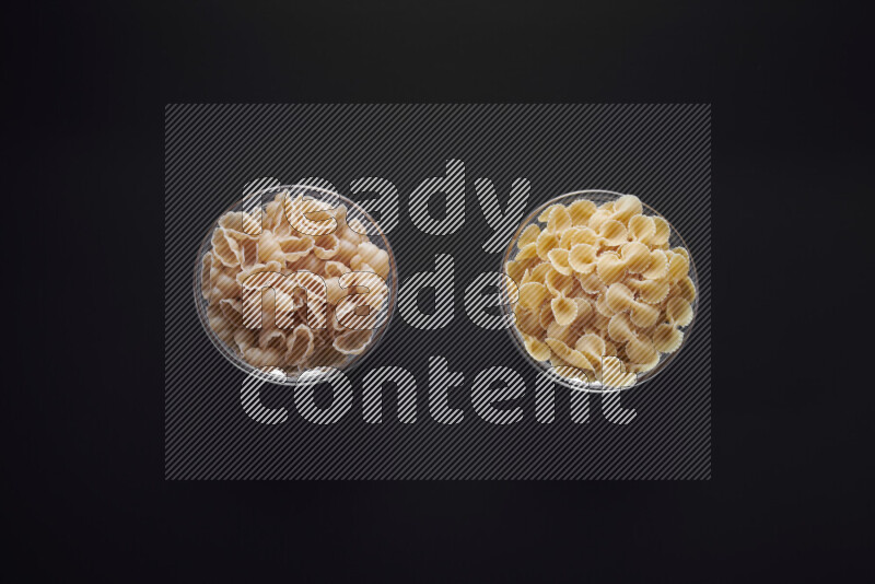 Different pasta types in glass bowls on black background