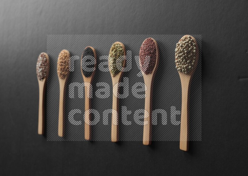 wooden spoons filled with white peppers, mustard seeds, black seeds, garden cress, cumin and flax on black flooring