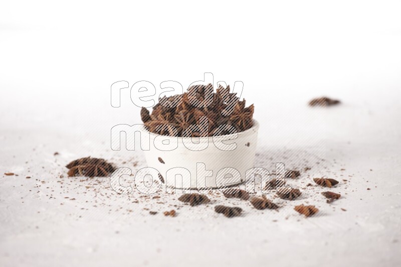 Star Anise in a white bowl and more of it sprinkled on white background