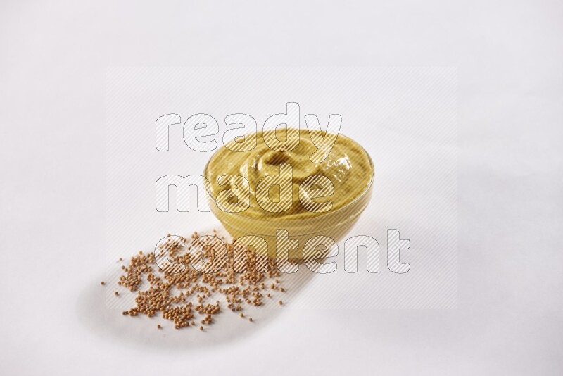 A glass bowl full of mustard paste with mustard seeds underneath on white flooring